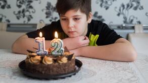 Teen boy looks thoughtfully at cake with candles on twelfth day of birth