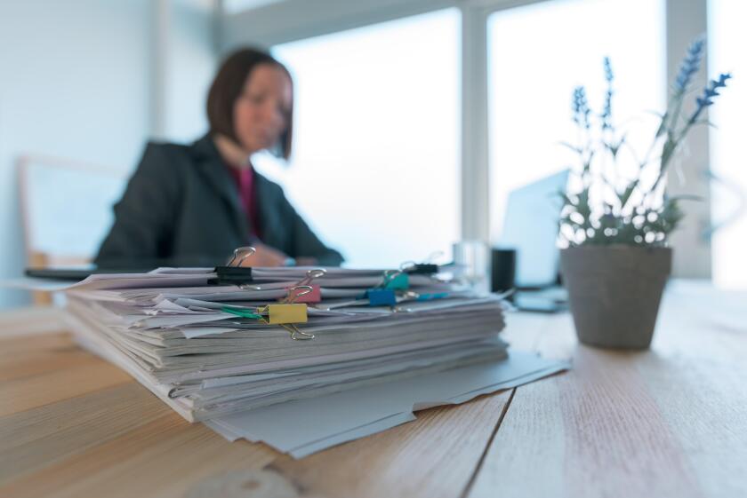 Busy businesswoman doing paperwork in office at the desk filled with papers and documentation