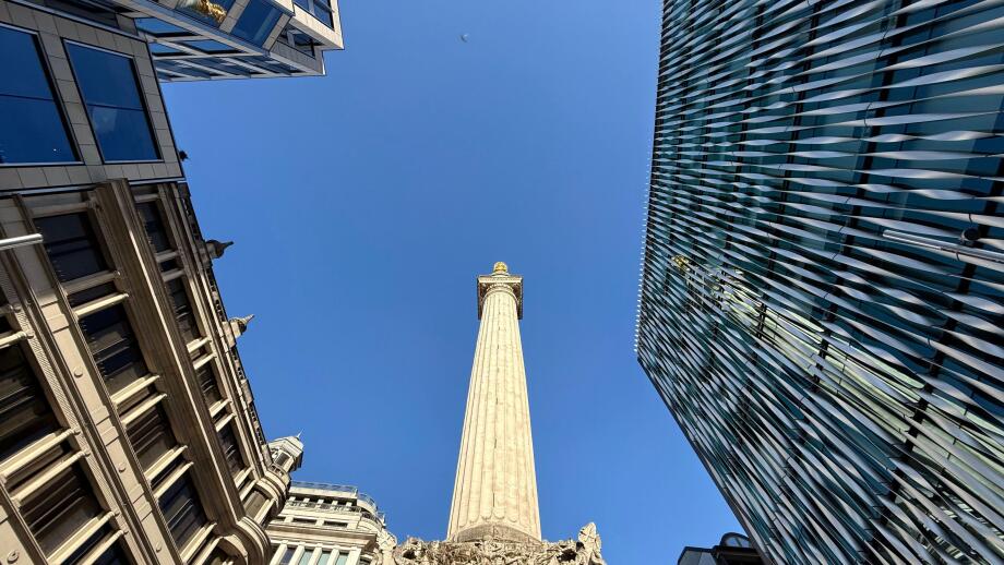 Looking up at The Monument against a vivid blue sky surrounded by office buildings in City of London