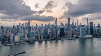 Aerial view of a vast cityscape with towering skyscrapers including the Empire State Building under a dramatic sky, New York, New York, United States.
