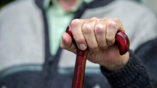 An elderly old age pensioner sits with his hands on a walking stick in a care home.