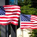 Two American flags wave vociferously in the wind in a suburban area
