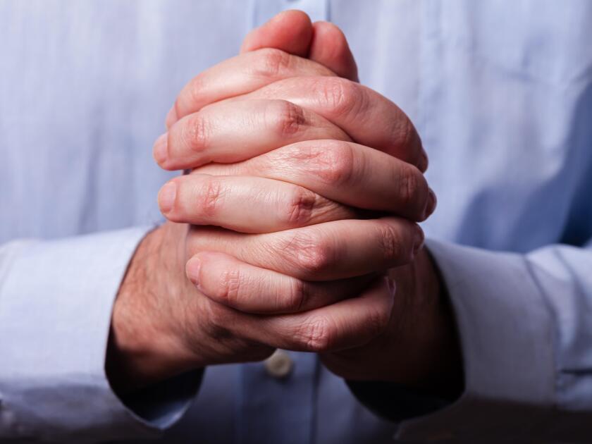 Close up or closeup of hands of faithful mature man praying. Hands folded, interlaced fingers in worship to god. Concept for religion, faith, prayer a