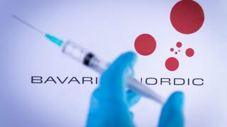 In this photo illustration a hand in medical gloves holds a syringe in front of Bavarian Nordic in Barcelona, Spain on September 2, 2021. Bavarian Nor