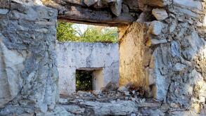 Abandoned old broken house with thick crumbling stone walls. Ruins of damaged rural home with an empty window frame. Weathered antique farmhouse with