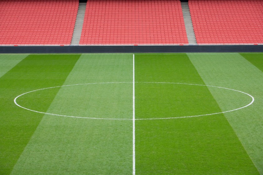 centre circle of a football pitch and bright red seating inside an empty football stadium.