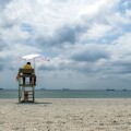 A lifeguard sitting on surveillance tower, front of the sea. Lifeguard Beach Chair. Beach lifeguard on duty. Cloudy sky.