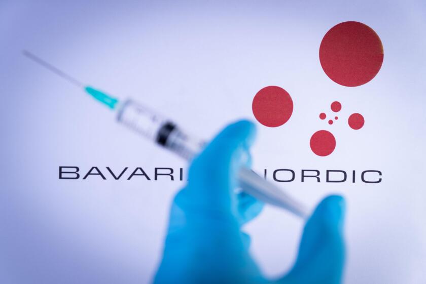 In this photo illustration a hand in medical gloves holds a syringe in front of Bavarian Nordic in Barcelona, Spain on September 2, 2021. Bavarian Nor