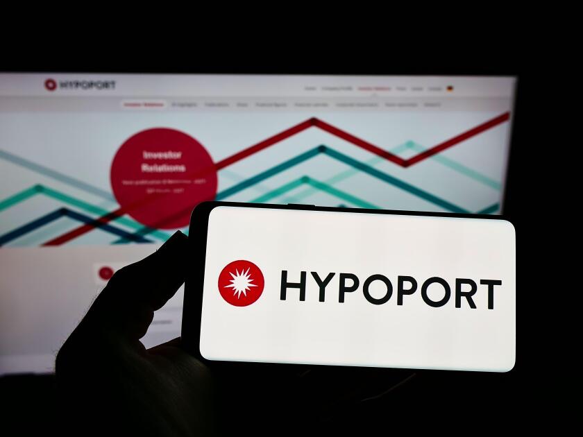 Person holding smartphone with logo of German technology company Hypoport SE on screen in front of website. Focus on phone display.