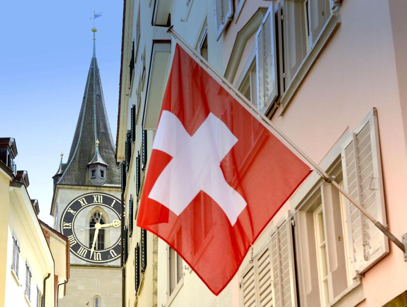Clock tower of the St. Peter Church and Swiss Flag on the facade building in Zurich, Switzerland