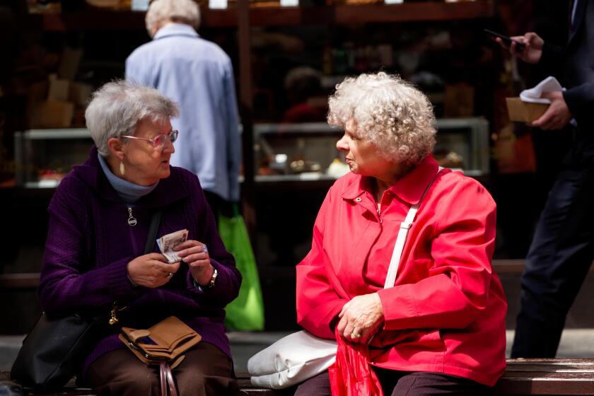 Two old age female pensioners sitting on a seat chatting about their pension money in Dundee, UK