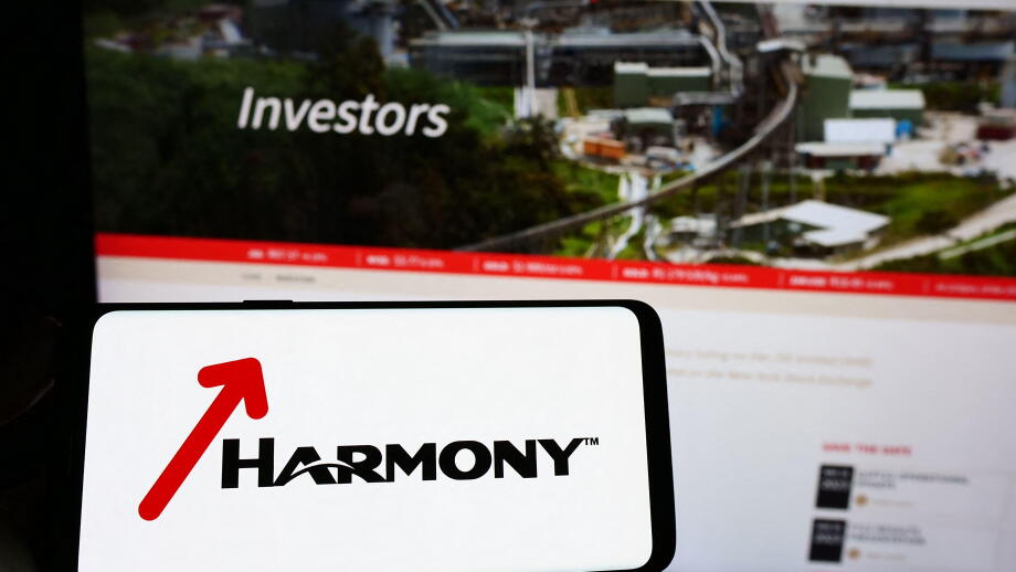 Person holding smartphone with logo of company Harmony Gold Mining Co. Ltd. on screen in front of website. Focus on phone display.