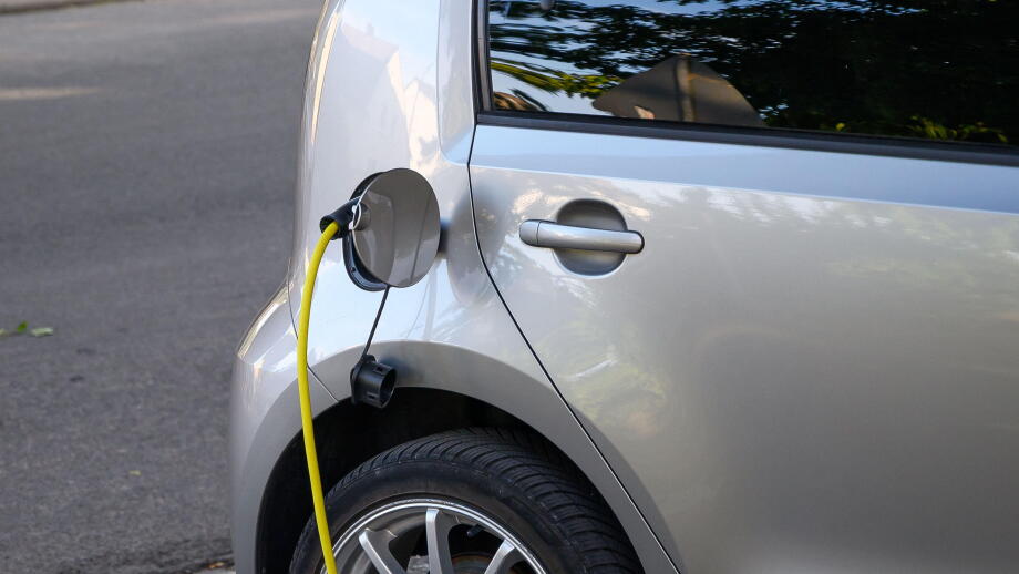 Silver electric car charging with a yellow cable plugged into its port.