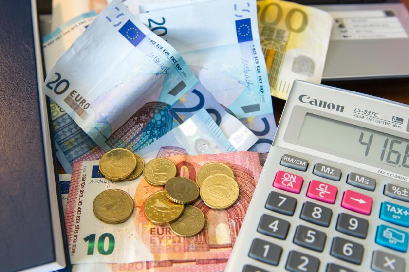 Various Euro notes and coins with a calculator, diary and laptop computer.