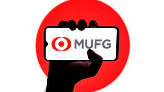 Smartphone with Mitsubishi UFJ Financial Group logo on screen in clenched hand on background of Japan flag