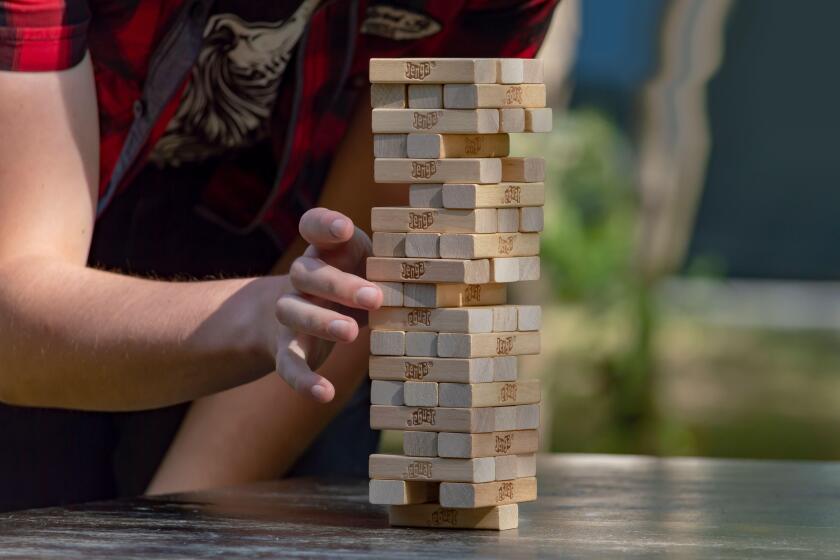 Guy sticks out wooden block from  tower of game jenga. Side front view. Concept. Surgut, Russia - September 25, 2019.