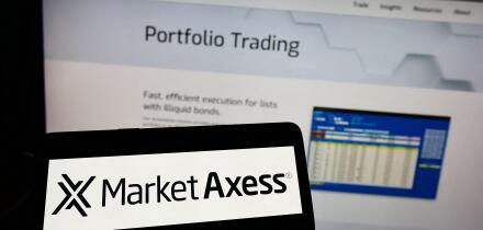 Person holding cellphone with logo of American financial company MarketAxess Holdings Inc. on screen in front of webpage. Focus on phone display.