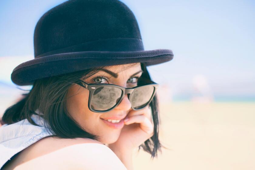 Portrait of smiling beautiful young woman in black hat. Model shooting on the beach.