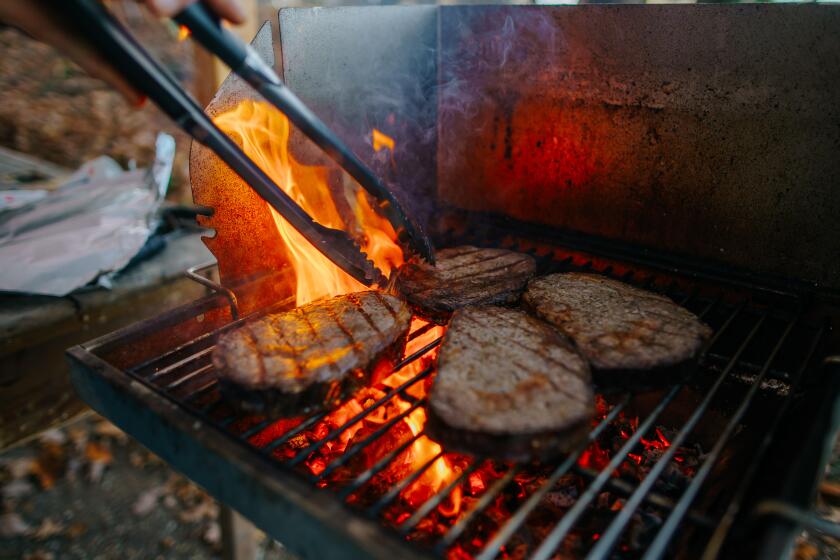 four well-done ribeye-steaks with high flames and barbecue tong on the grill
