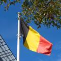 Belgian flag swaying in the wind against blue sky and trees. Flag of Belgium near train station. Flag day celebration. Embassies and consulates