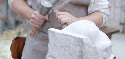 Close up of young sculptor hands working on his marble sculpture in his workshop with hammer and chisel