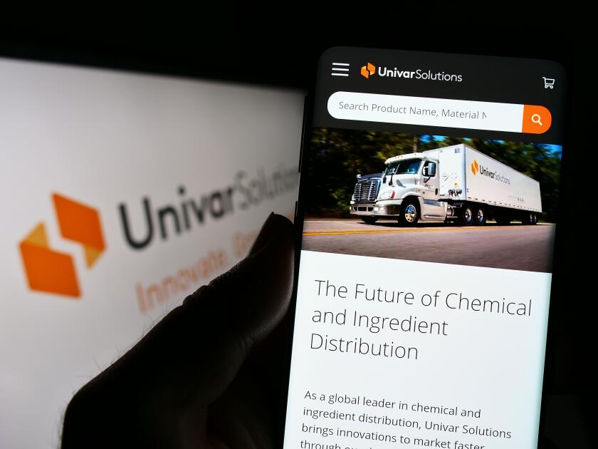 Person holding cellphone with website of US distribution company Univar Solutions Inc. on screen with logo. Focus on center of phone display.