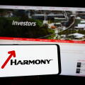 Person holding smartphone with logo of company Harmony Gold Mining Co. Ltd. on screen in front of website. Focus on phone display.