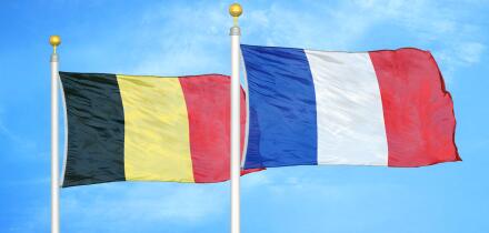 Belgium and France two flags on flagpoles and blue cloudy sky