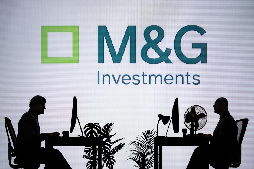The M&G Investments logo is seen on an LED screen in the background while two silhouetted people work in an office environment (Editorial use only)
