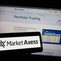 Person holding cellphone with logo of American financial company MarketAxess Holdings Inc. on screen in front of webpage. Focus on phone display.
