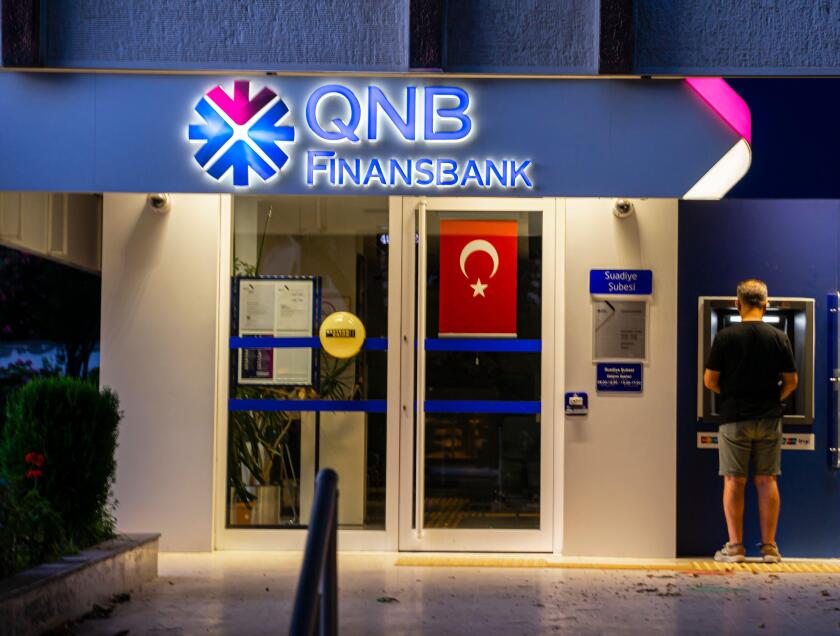 Turkish banks - QNB Finansbank  - colorful bank buildings illuminated.  Kadikoy Istanbul Turkey. Young man withdrawing money in ATM