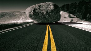 Yellow lane divider leading up to a boulder blocking the road