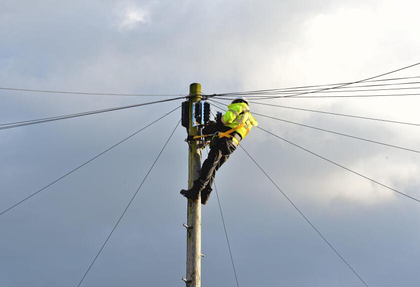 A British Telecoms engineer installing fibre optic cable at the top of a telephone pole England UK