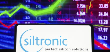 In this photo illustration the Siltronic AG logo seen displayed on a smartphone screen, with graphic representation of the stock market in the backgro