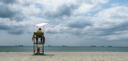 A lifeguard sitting on surveillance tower, front of the sea. Lifeguard Beach Chair. Beach lifeguard on duty. Cloudy sky.