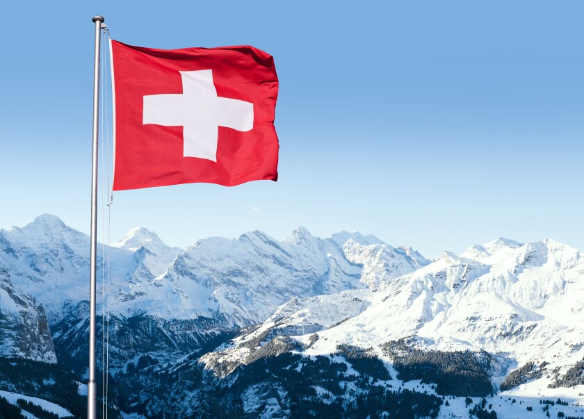 The flag of Switzerland fluttering in the wind with the Bernese Alps in the background, Grindelwald, Switzerland.