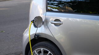 Silver electric car charging with a yellow cable plugged into its port.