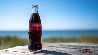 A coca-cola bottle against a sea and blue sky background in summer