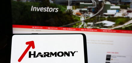 Person holding smartphone with logo of company Harmony Gold Mining Co. Ltd. on screen in front of website. Focus on phone display.