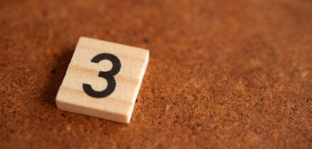 Wooden tile with the prime number 3 on a rustic brown surface, mathematical concept with copy space for education and numeracy