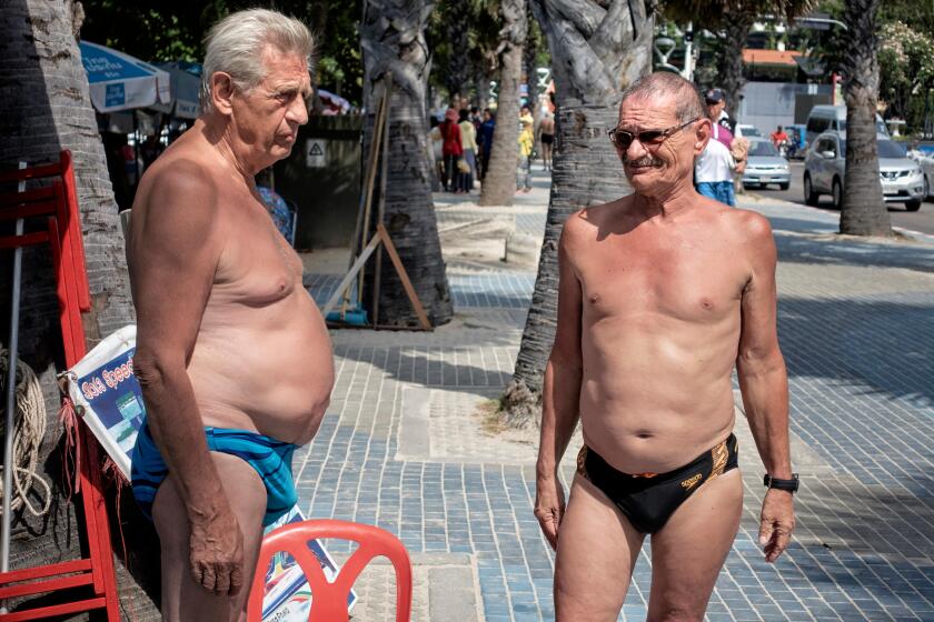 Two mature men with pronounced stomachs and wearing speedos swimming trunks chatting on the street