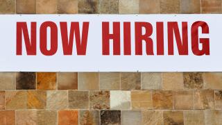 NOW HIRING sign on tiled wall.