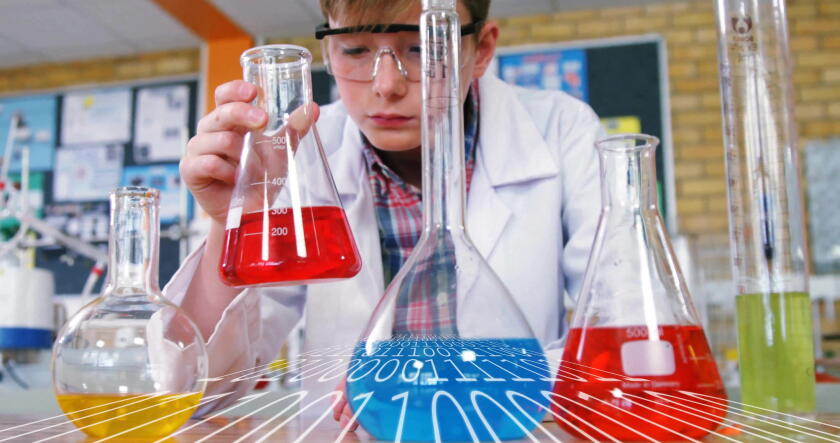 Examining red liquid in conical flask, boy wearing lab coat and goggles at school lab