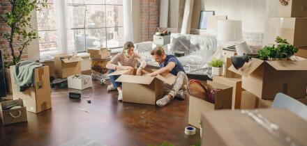 Happy Young Homeowners Moving In: Happy Couple Sitting on the Floor of the Newly Purchased Apartment Unpacking Cardboard Boxes. Mortgage Loan, Real Estate, Home Sweet Home for Young Family