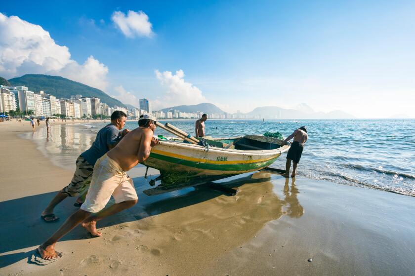 RIO DE JANEIRO - APRIL 4, 2016: Brazilian fishermen launch a brightly painted fishing boat on Copacabana Beach.