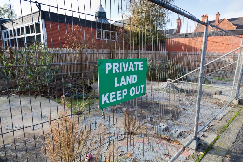 Derelict building plot surrounded by metal wire fencing and 'keep out' notice.