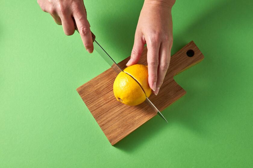 A woman cuts a yellow ripe lemon in half with knife on a wooden board on a green background. Top view.