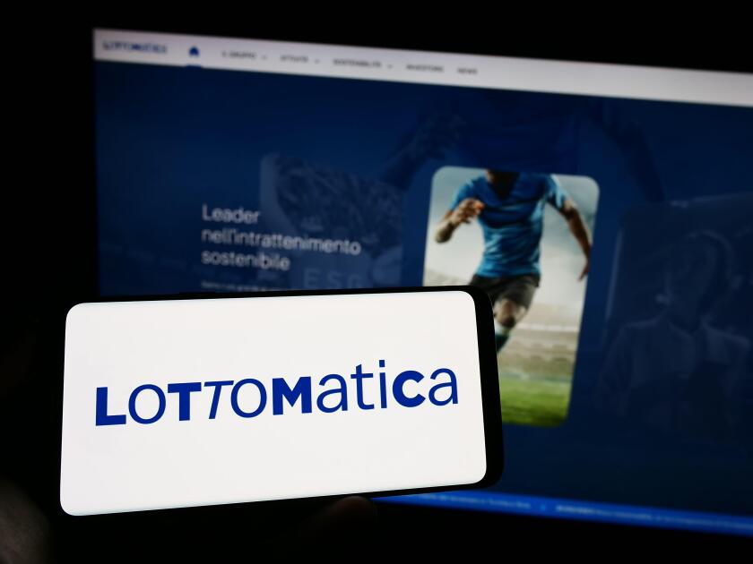 Person holding cellphone with logo of Italian gambling company Lottomatica SpA on screen in front of business webpage. Focus on phone display.