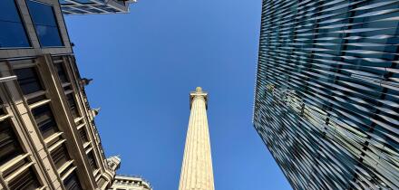 Looking up at The Monument against a vivid blue sky surrounded by office buildings in City of London