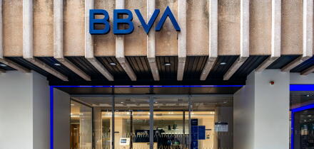 The BBVA bank branch in Cartagena, Spain, featuring a concrete ribbed facade, blue logo, and glass sliding doors illuminated by purple neon lights.